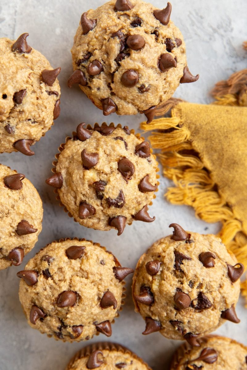 Chocolate Chip Banana Oat Muffins on a surface with a golden napkin to the side. Ready to eat.