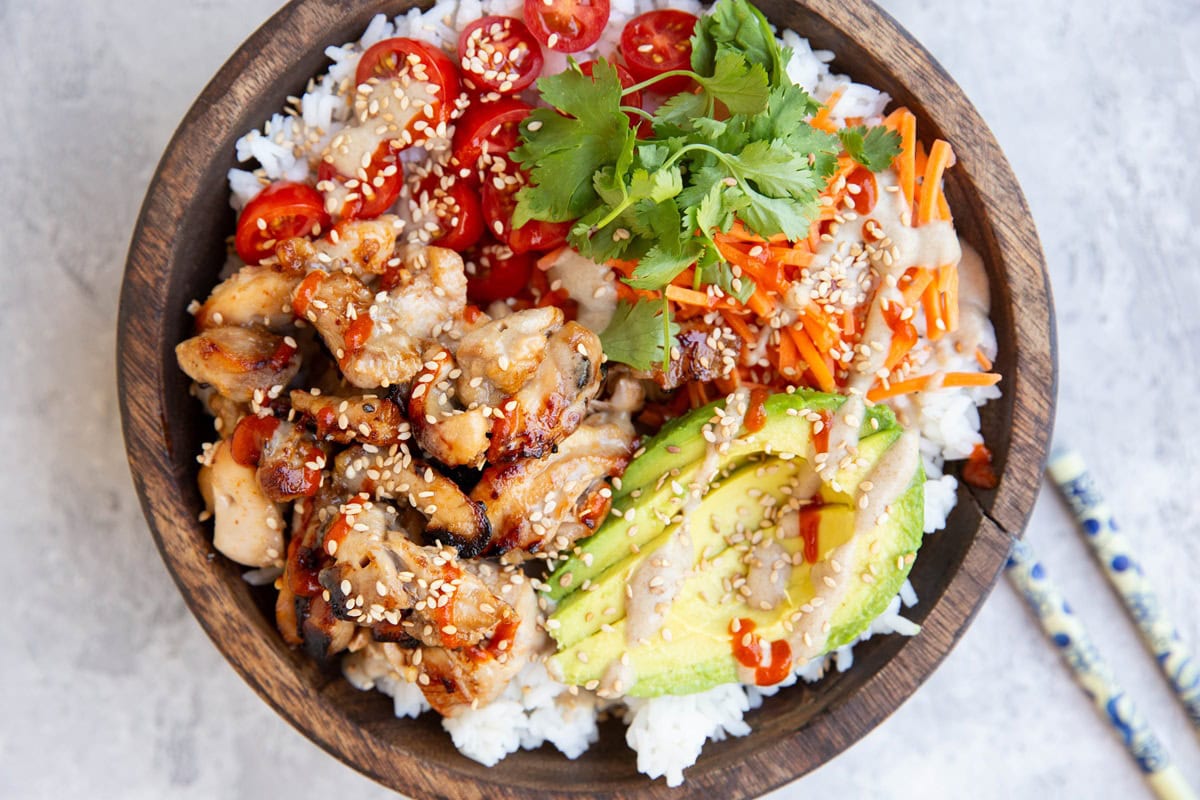 Bowl of chicken, rice, fresh vegetables, and peanut sauce.