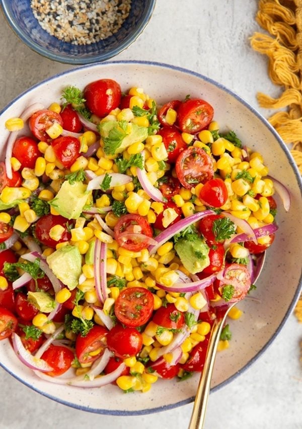 Bowl full of corn and tomato salad with a golden spoon, ready to serve