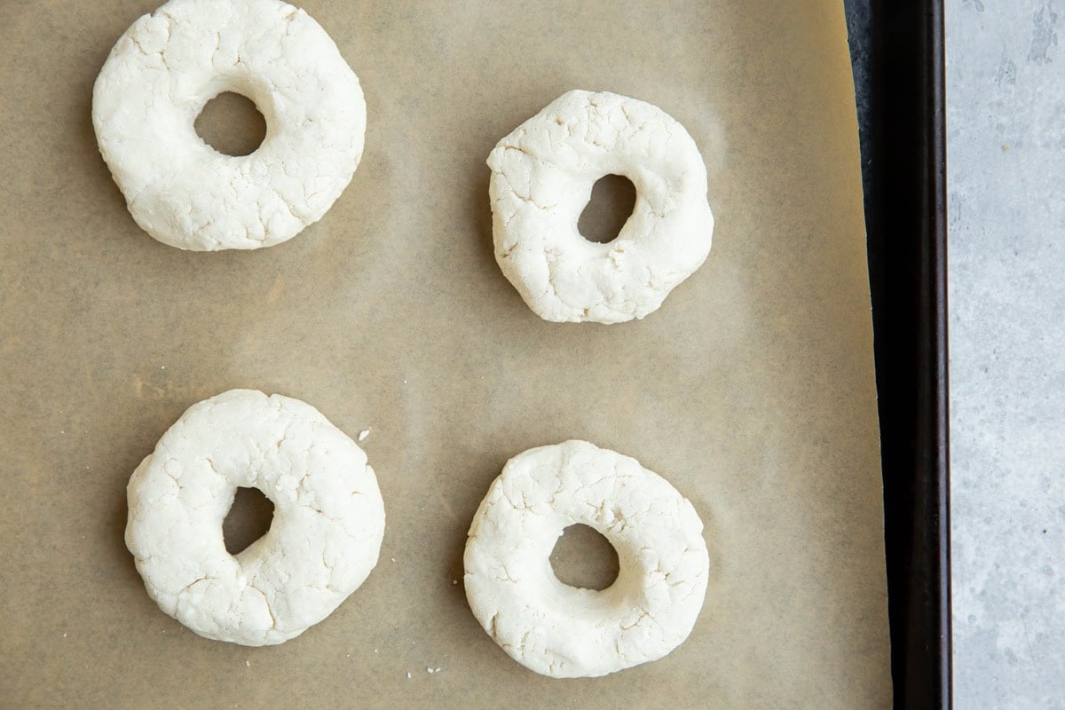 Four bagel doughs on a baking sheet, ready to go into the oven.