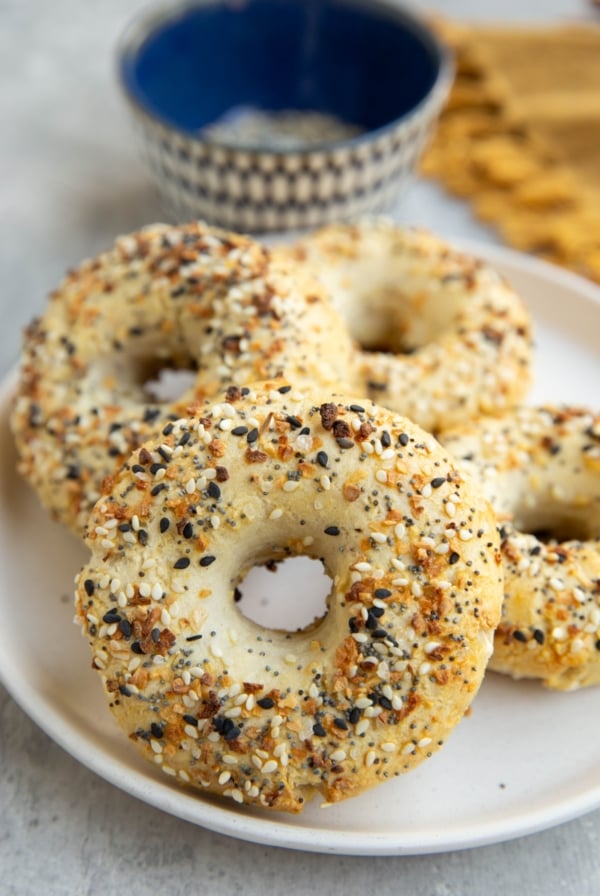 Four homemade bagels on a plate with a bowl of everything bagel seasoning in the background.
