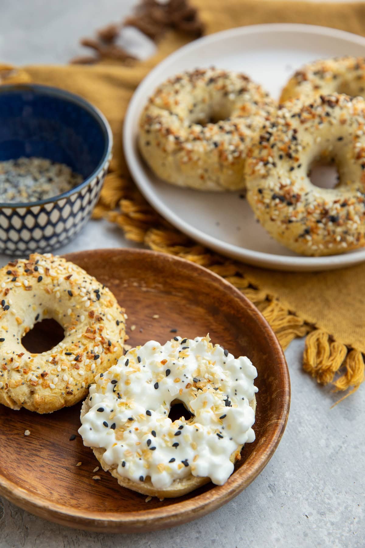 Plate with a bagel sliced in half coated with cottage cheese sprinkled with everything bagel seasoning. A plate in the background with more bagels.