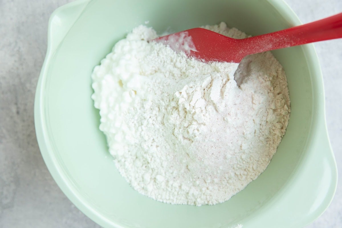 Mixing bowl with cottage cheese, flour, and salt inside with a rubber spatula.