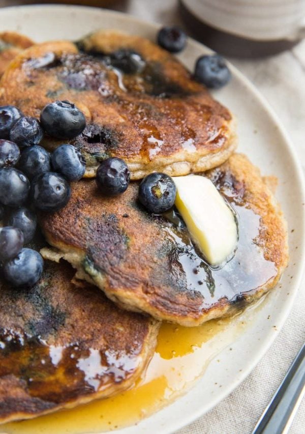 Almond flour pancakes on a plate with fresh blueberries, melted butter, and honey. A fork to the side, ready to serve.