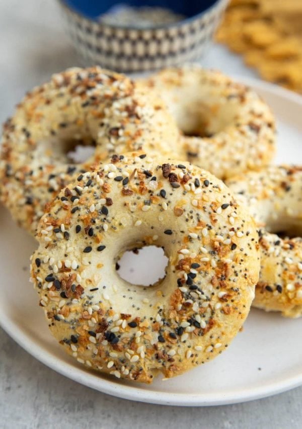 Four homemade bagels on a plate with a bowl of everything bagel seasoning in the background.