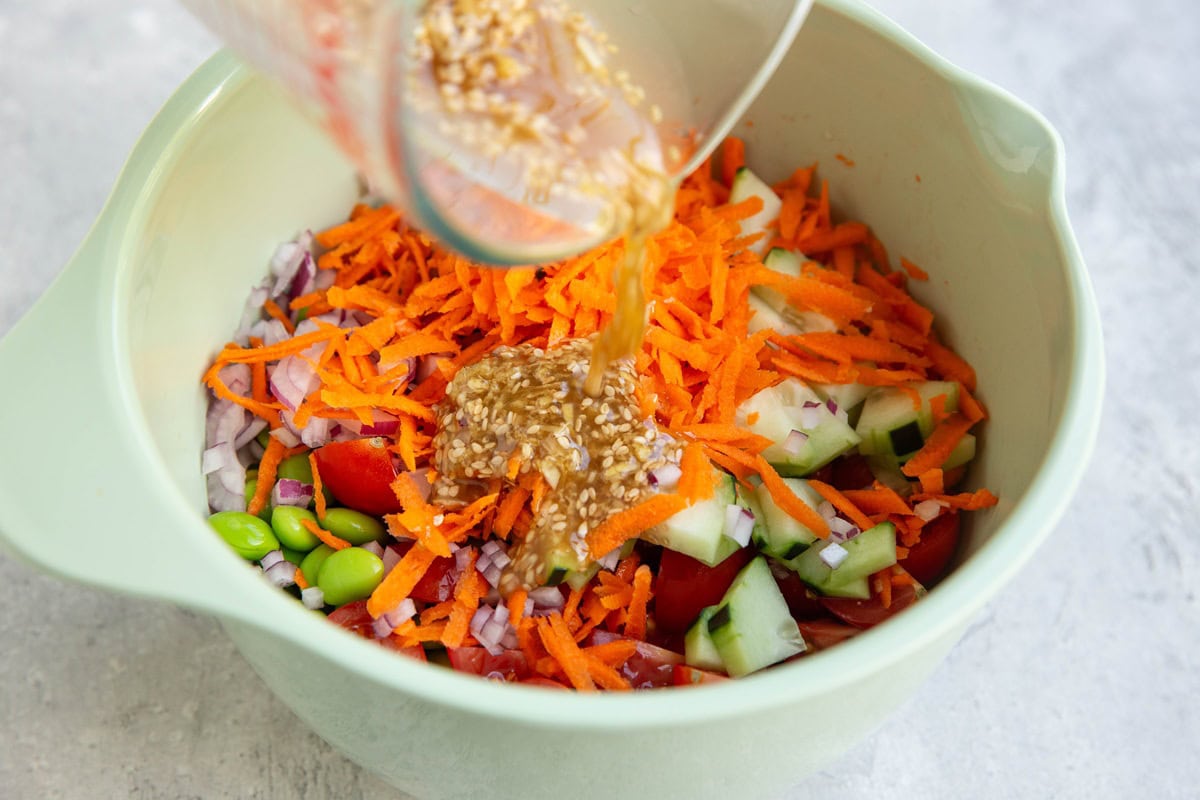 Pouring dressing into a bowl full of fresh vegetables.