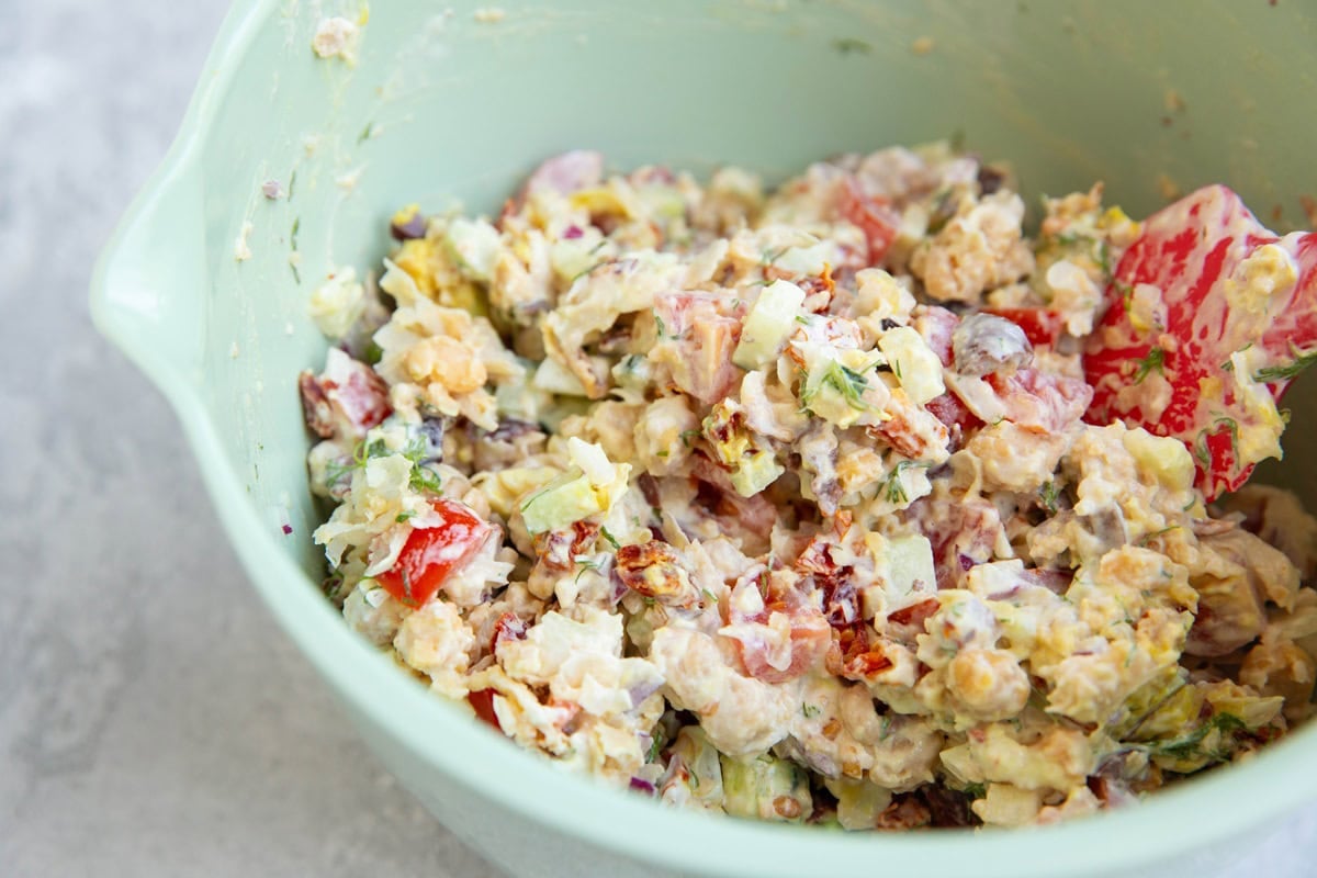 Large bowl full of Greek chickpea tuna salad with a rubber spatula inside, all mixed up and ready to eat.