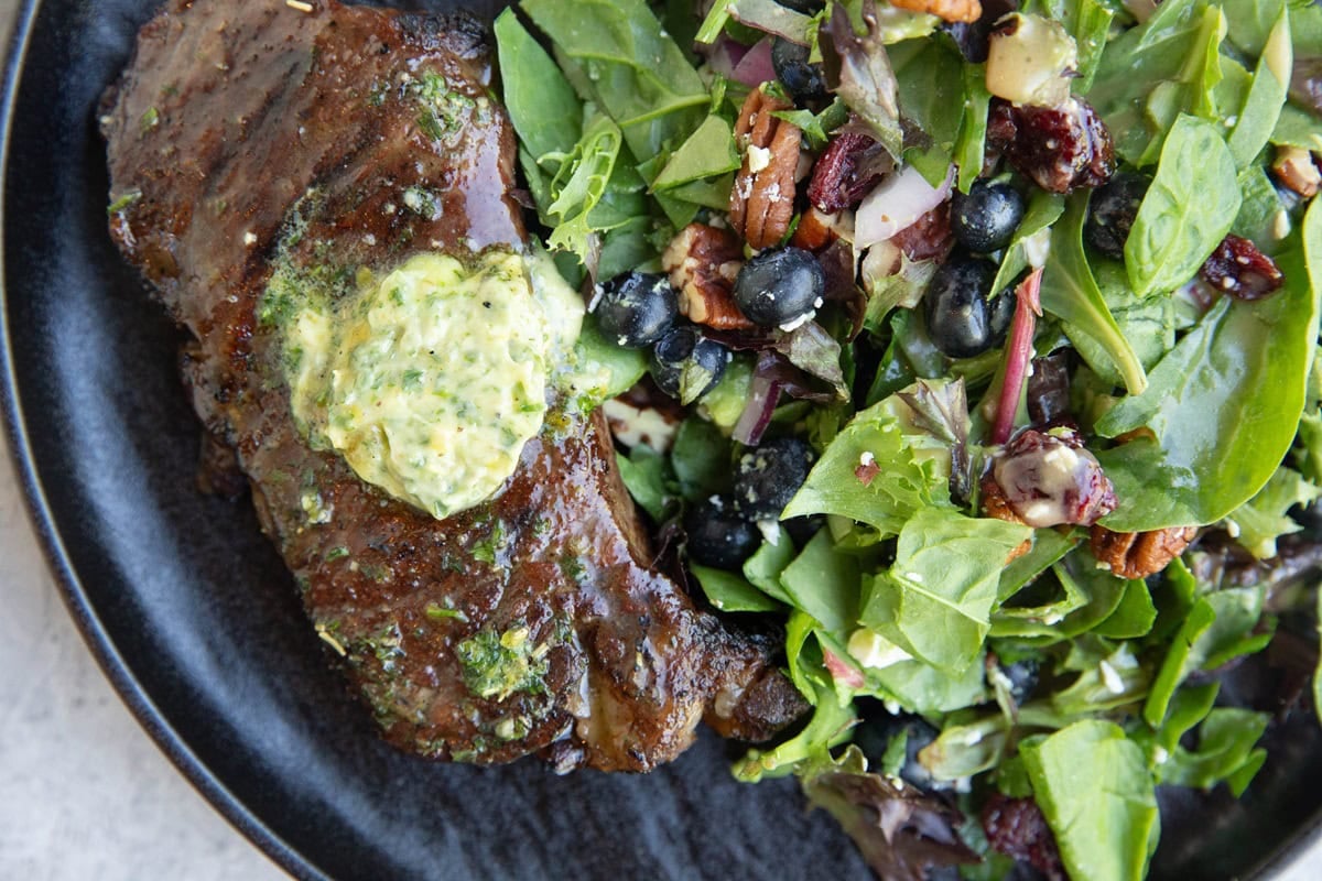 New York strip steak with compound butter on top and a side salad on a plate.