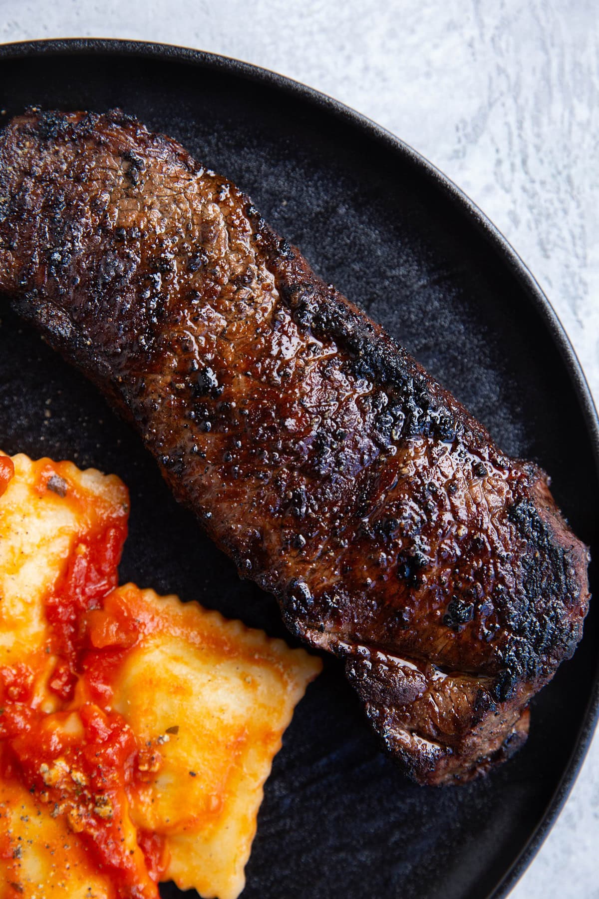 Grilled NY strip steak on a plate next to raviolis, ready to serve.
