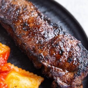 Plate of grilled new york strip steak with raviolis as a side dish.