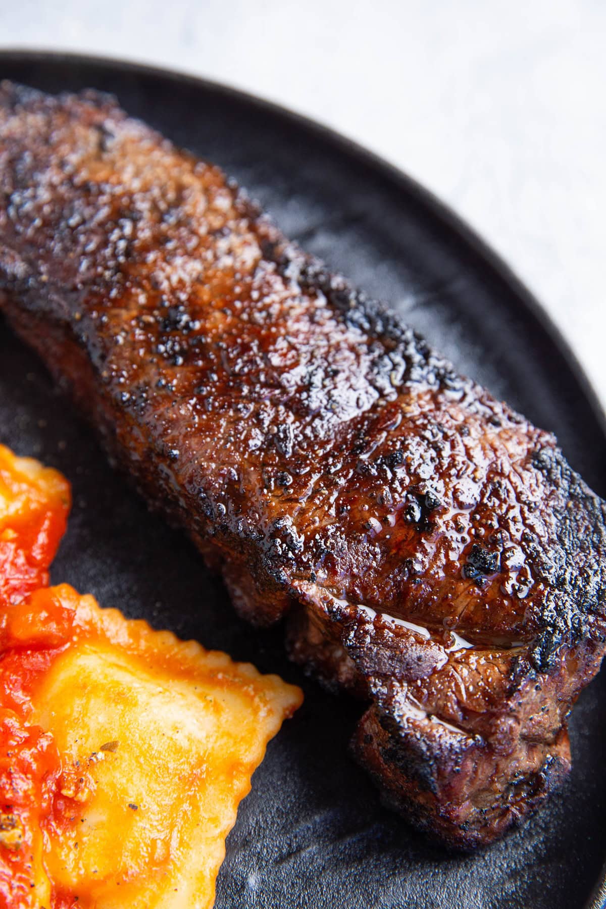 Plate of grilled new york strip steak with raviolis as a side dish.