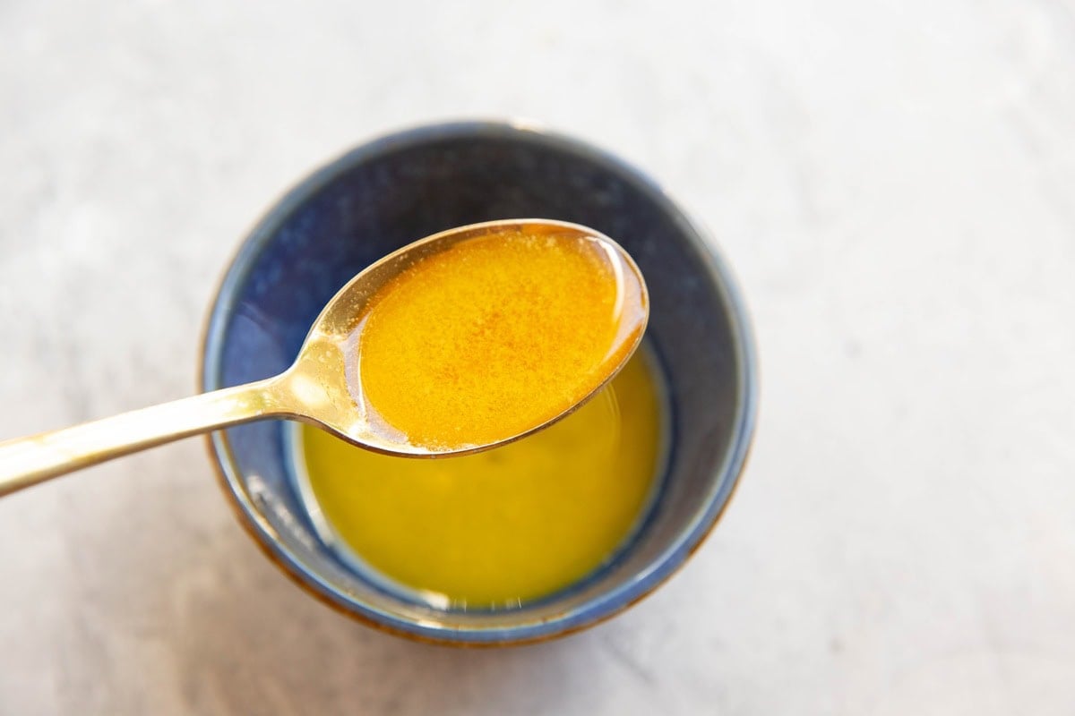 Blue bowl full of butter and honey mixed together with a golden spoon spooning out some of the honey butter.