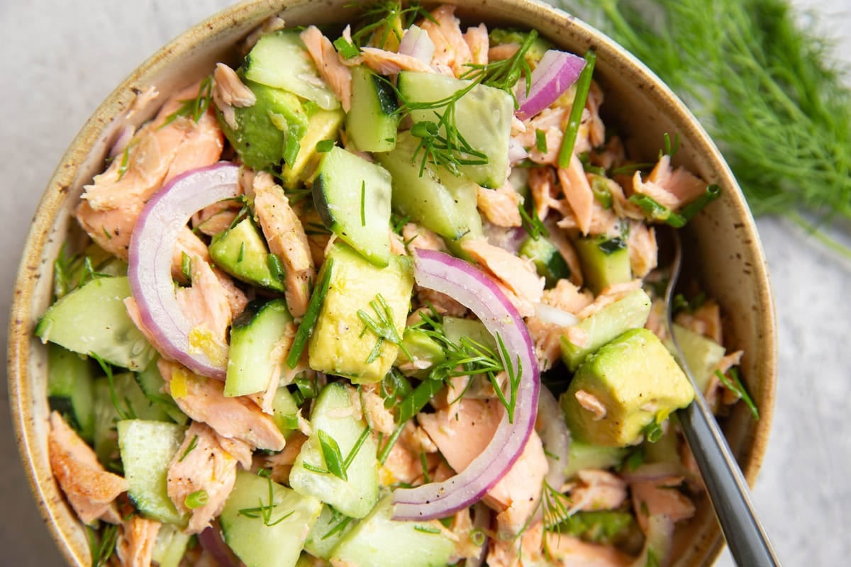 Bowl full of salmon and avocado salad with a fork to the side, ready to serve.