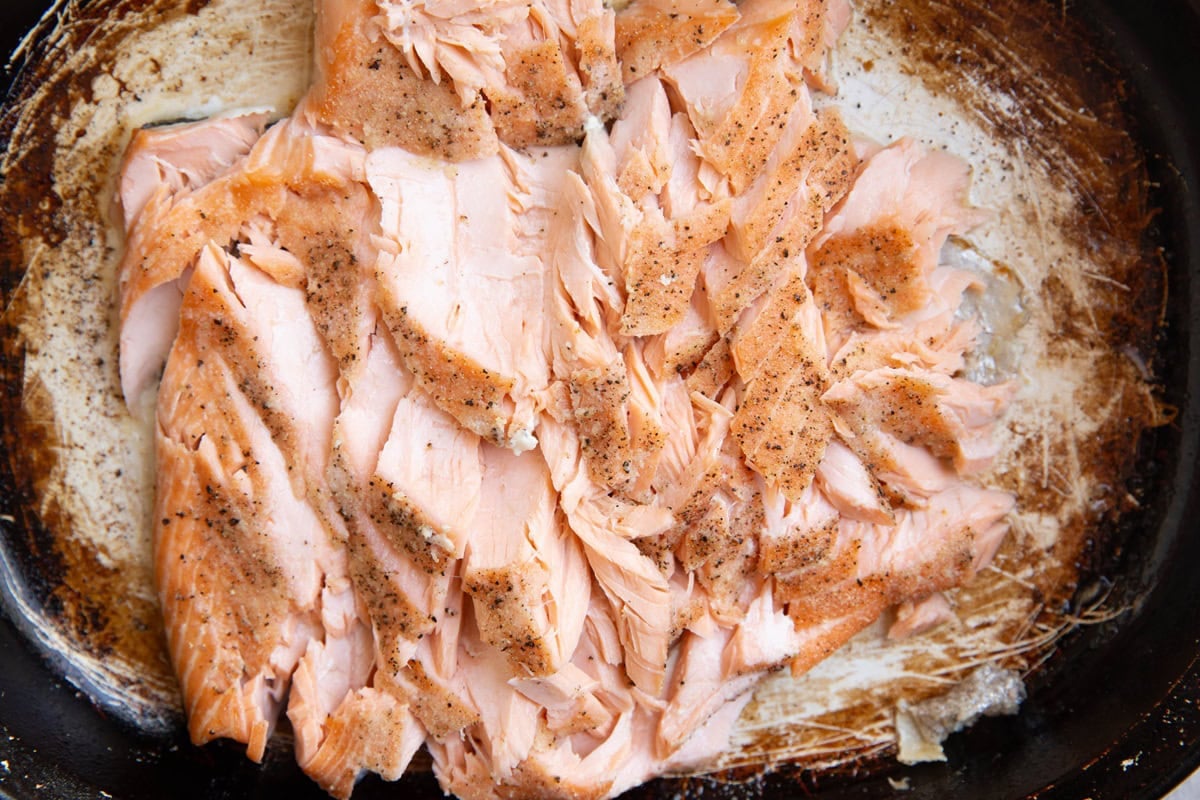 Cooked salmon in a casserole dish, flaked into bite-sized pieces to use in salmon salad.