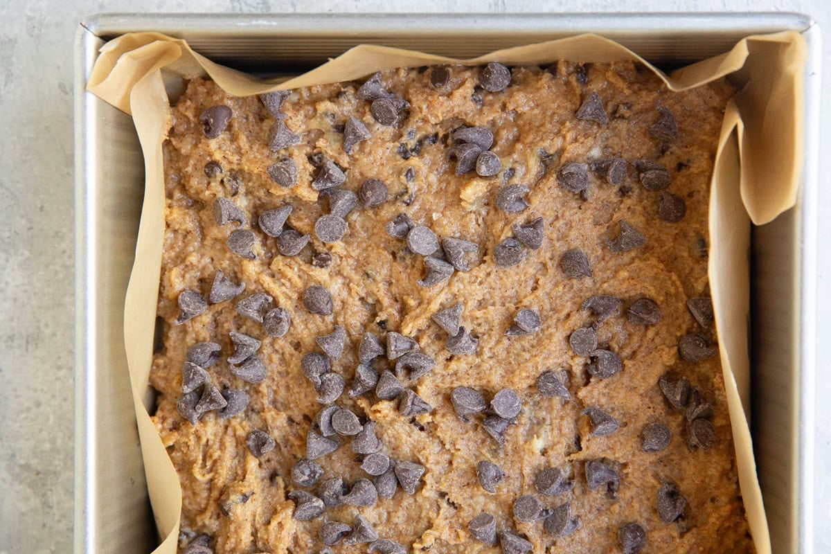 Banana bar batter in a baking dish lined in parchment paper, ready to go into the oven.