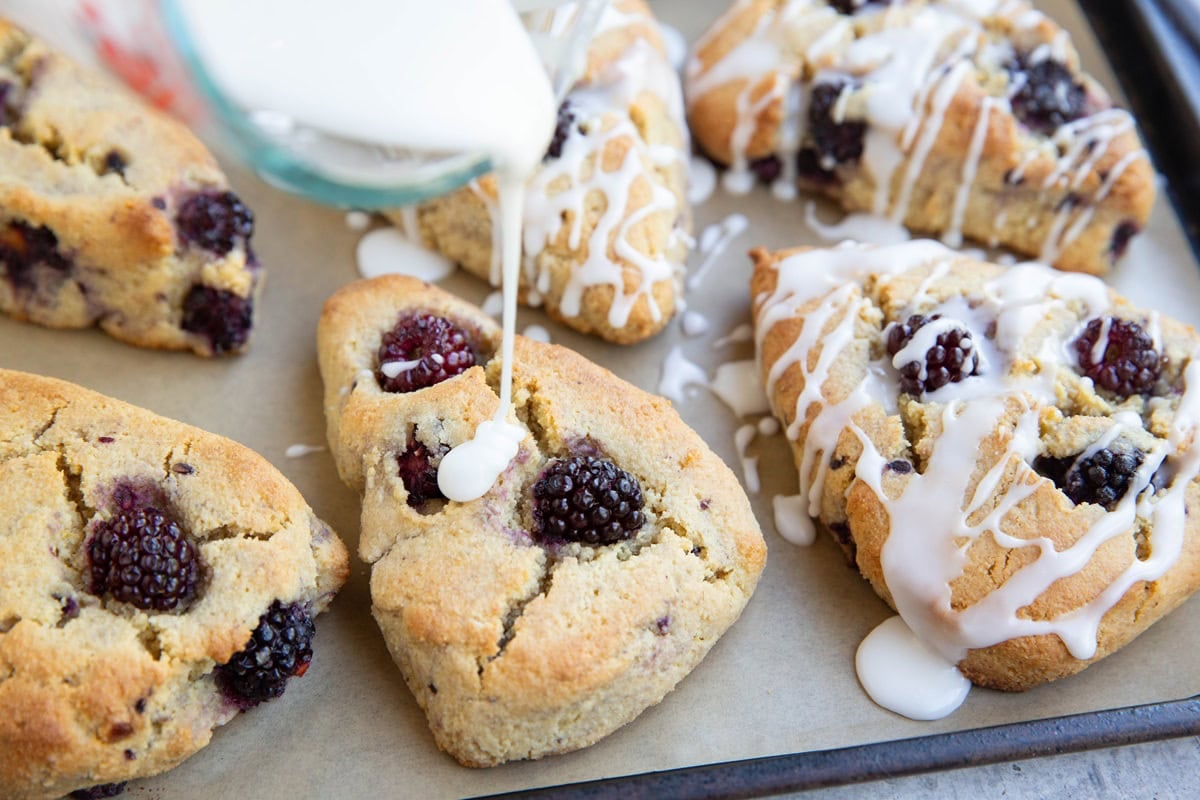 Drizzling powder sugar glaze over blackberry scones.
