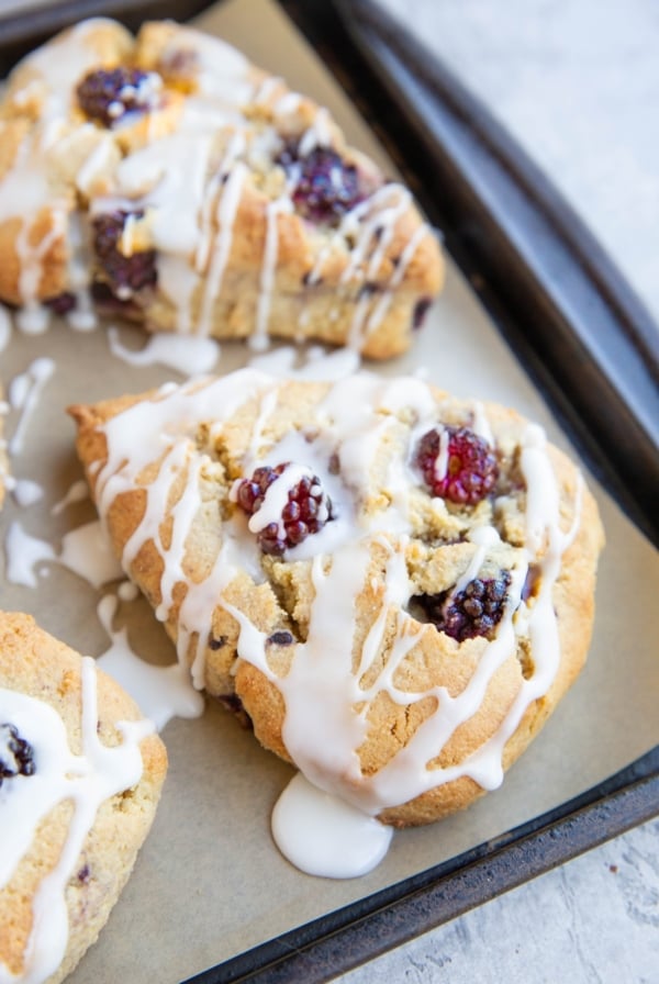 Baking sheet with blackberry almond flour scones drizzled with a simple glaze.