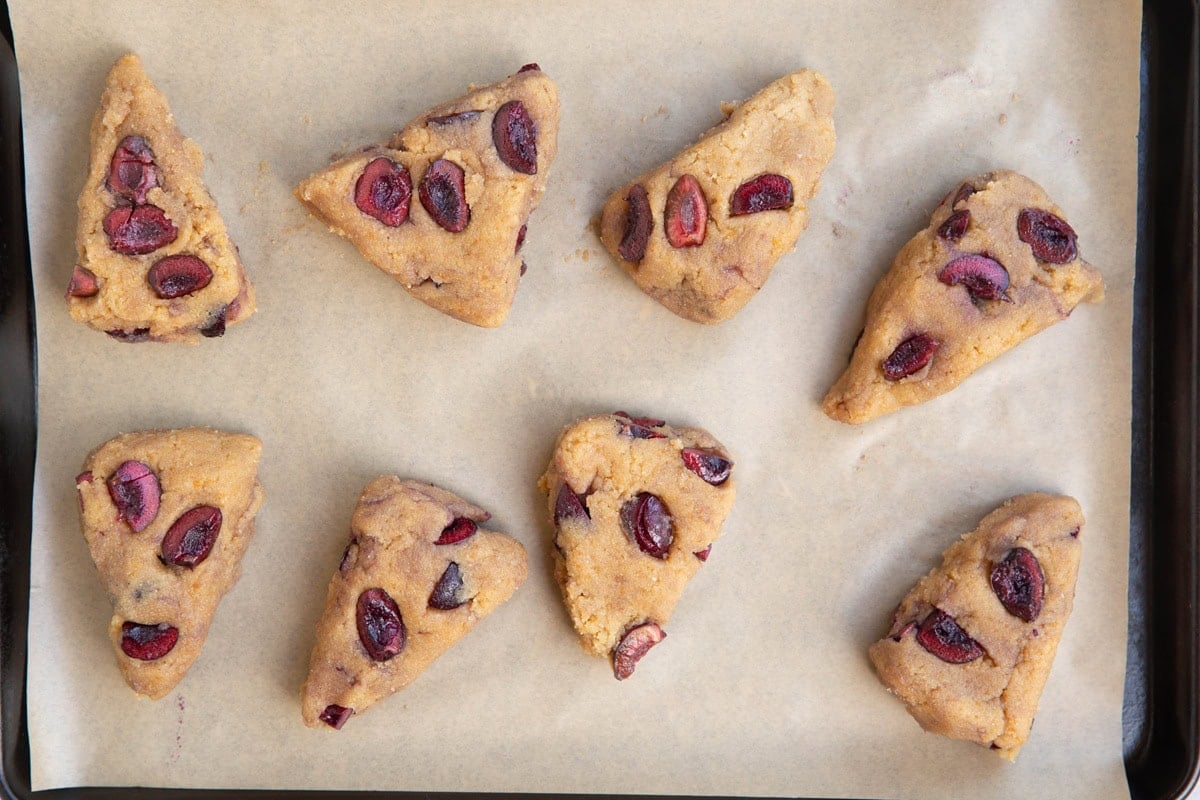 Cherry scone dough on a baking sheet lined with parchment paper, ready to go into the oven.