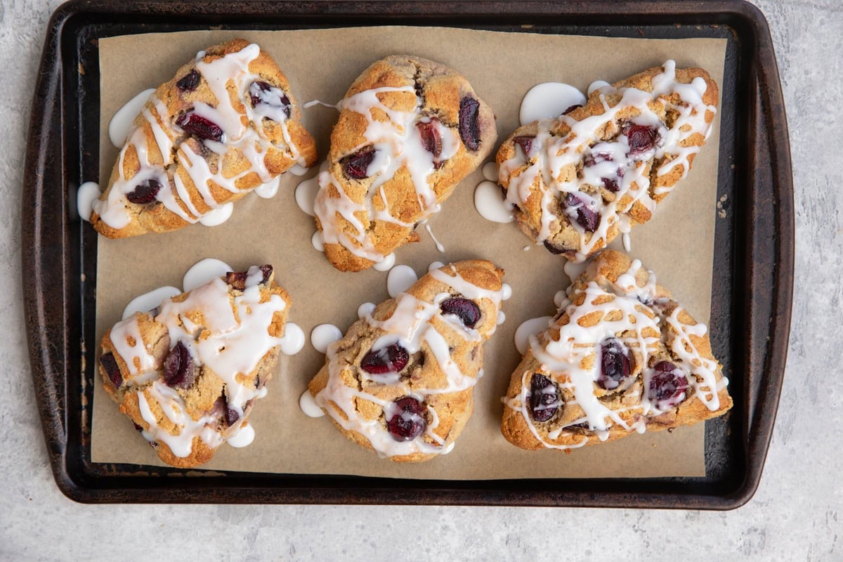 Baking sheet with 8 cherry scones drizzled with glaze, fresh out of the oven.