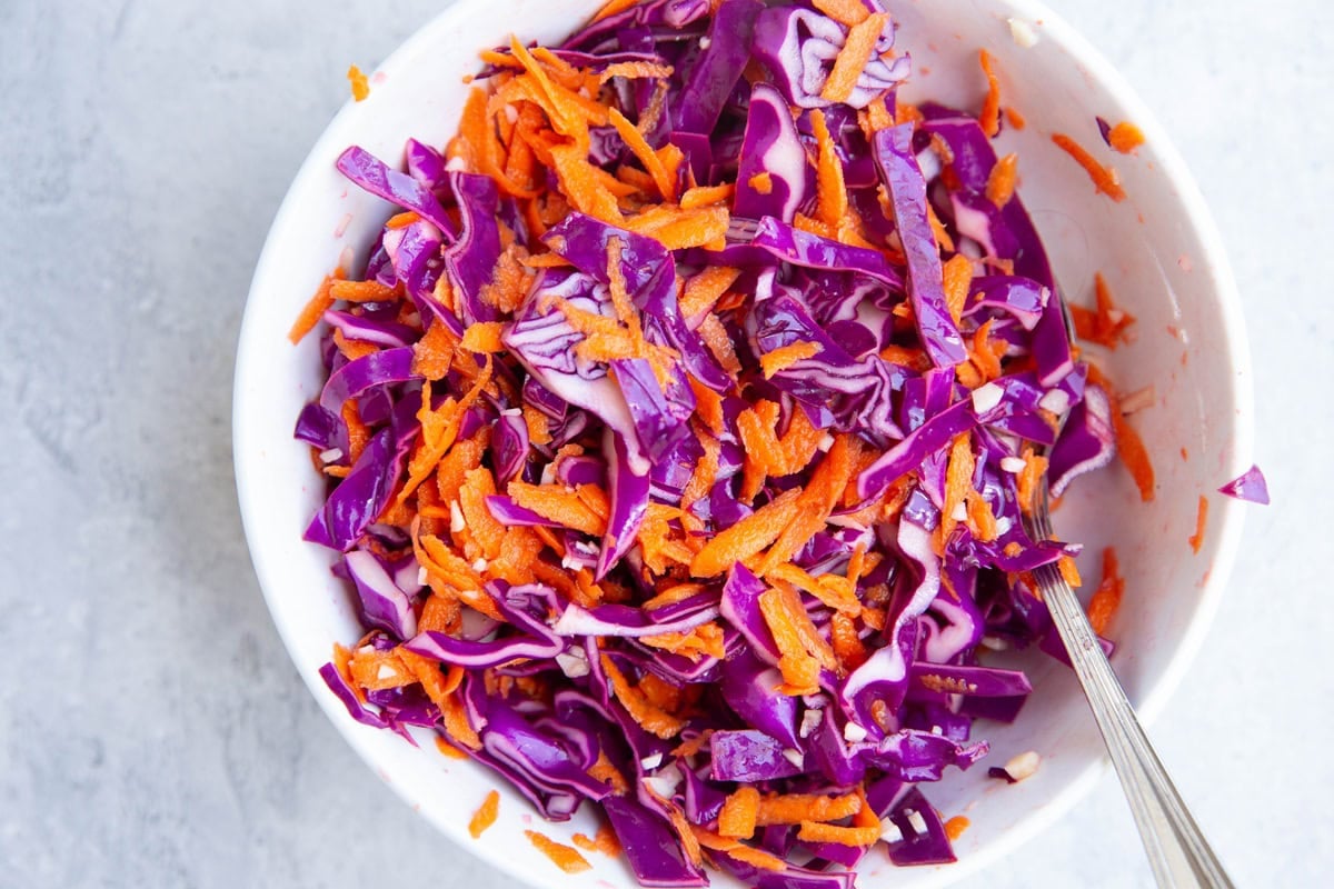 cabbage slaw in a bowl all mixed up with a serving spoon, ready to use.