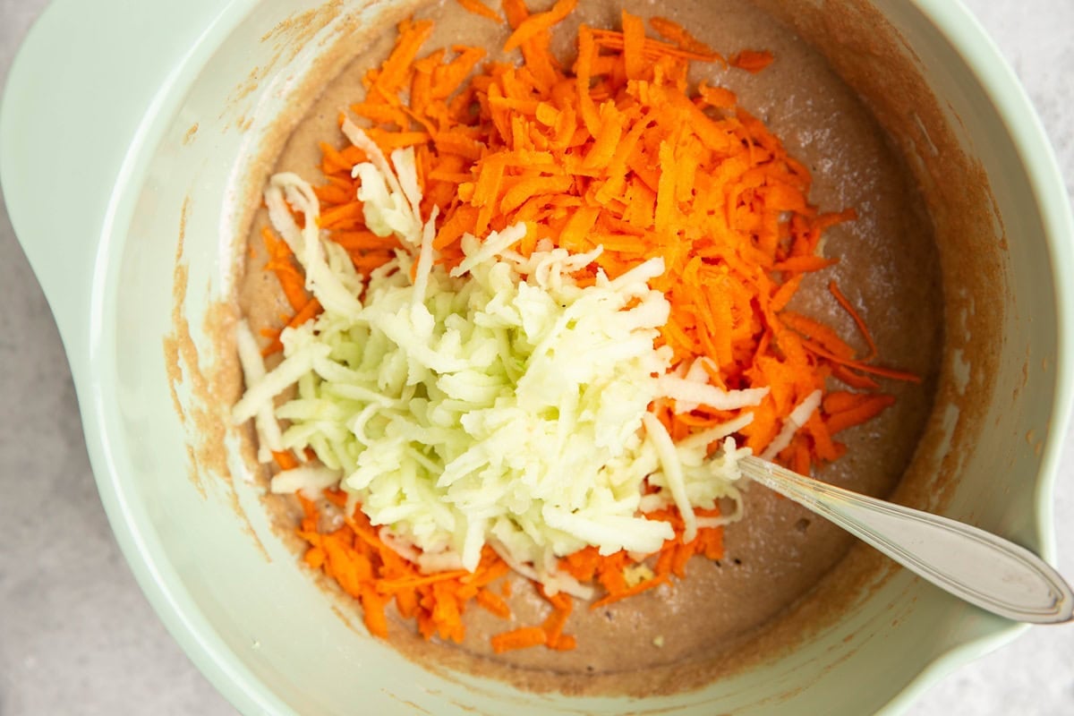 Mixing bowl full of quick bread batter with grated carrot and apple on top.
