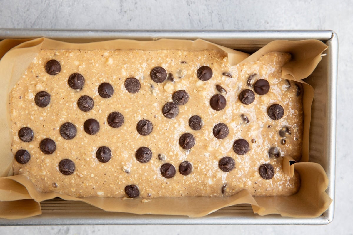 parchment lined loaf pan with chocolate chip bread batter inside, ready to be baked.