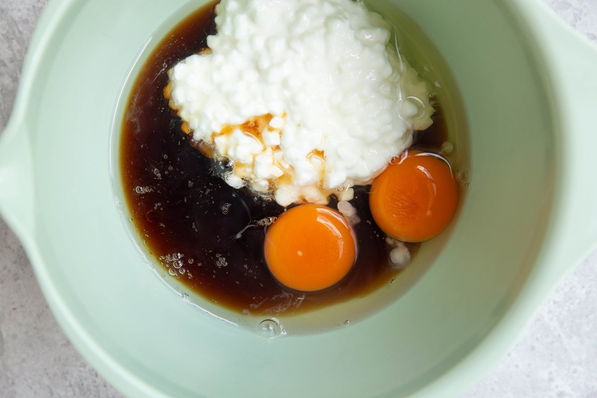 Cottage cheese, pure maple syrup, oil, and eggs in a large mixing bowl, ready to be mixed.
