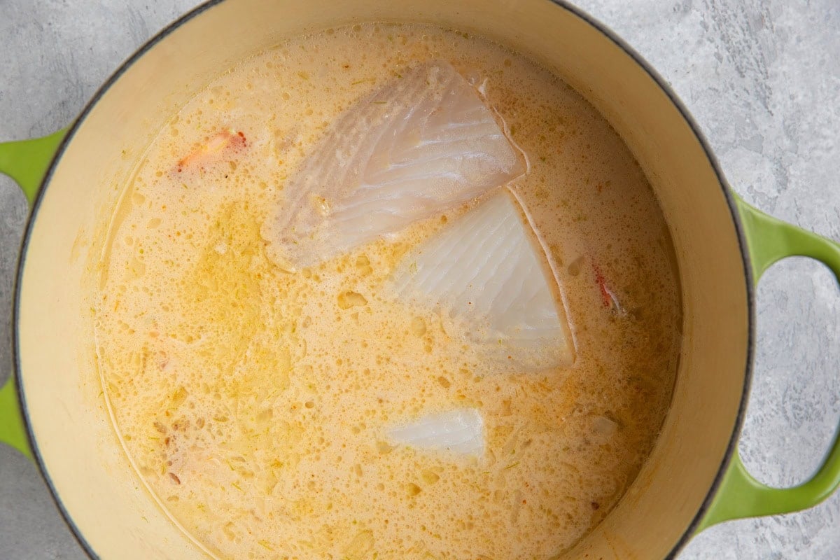 Large pot of coconut lime broth with fresh fish filets inside, ready to cook.