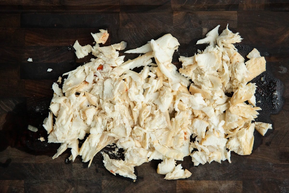 Cutting board with cooked white fish broken into small chunks.