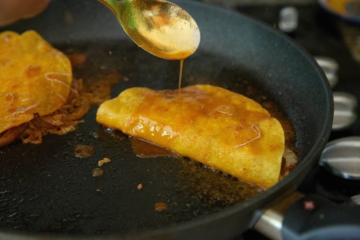 Spoon pouring sauce over a taco in a skillet to make chicken birria tacos.