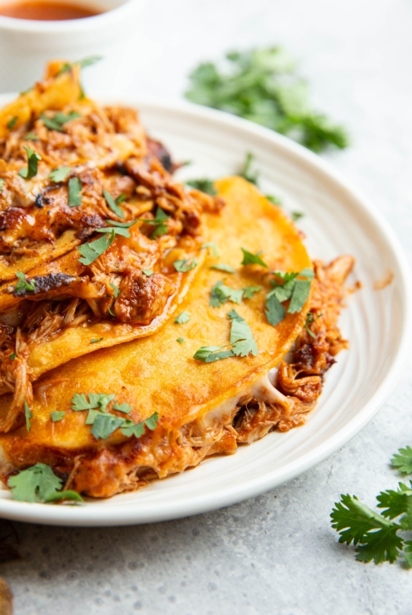 Four chicken birria tacos on a plate with a closeup so you can see the melted cheese and moist chicken. Sprinkled with fresh cilantro.