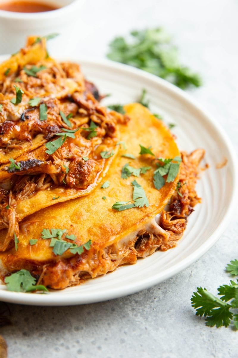 Four chicken birria tacos on a plate with a closeup so you can see the melted cheese and moist chicken. Sprinkled with fresh cilantro.