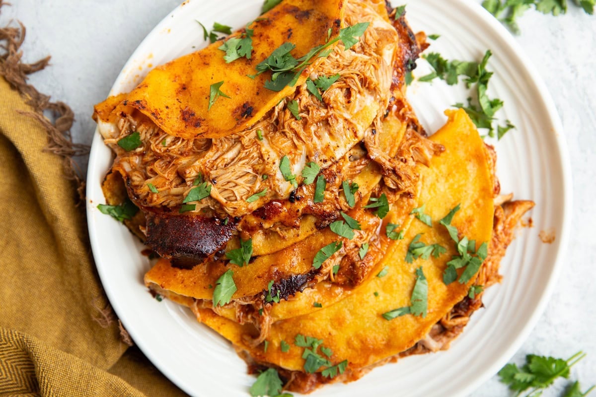 Chicken birria tacos on a plate sprinkled with chopped fresh cilantro and a golden napkin to the side.