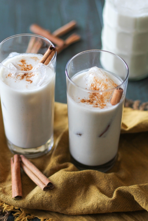 Homemade horchata in two glasses with cinnamon sticks and ice cubes inside and a golden napkin.