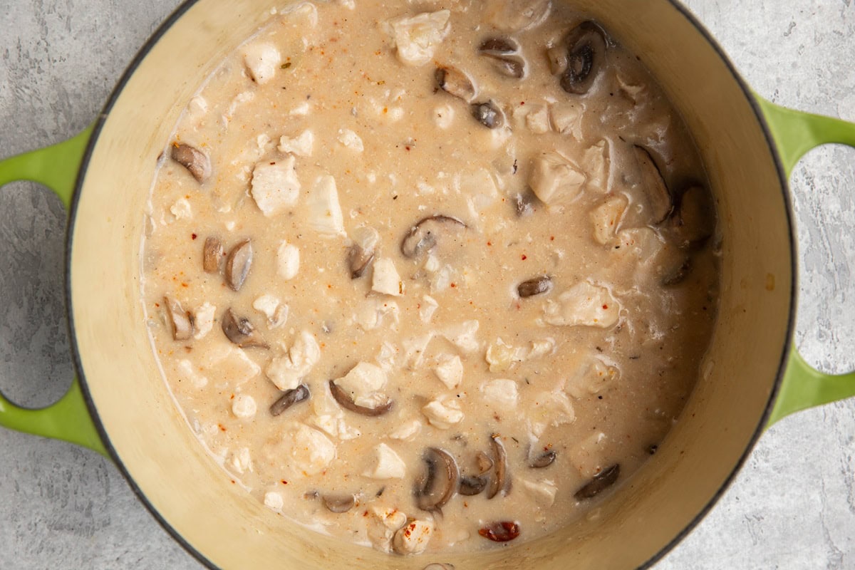 Large pot full of creamy chicken and mushrooms with a lot of creamy sauce.