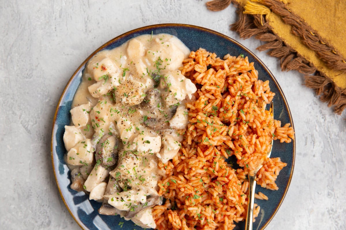Blue plate of creamy chicken with Spanish rice and a fork for serving.