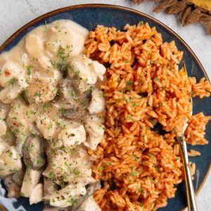 Chicken in a creamy sauce on a blue plate with Mexican rice and a golden fork, ready to serve.