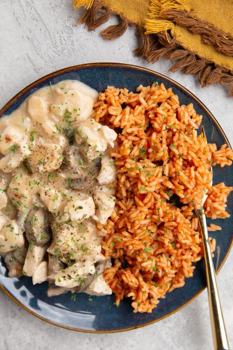 Chicken in a creamy sauce on a blue plate with Mexican rice and a golden fork, ready to serve.