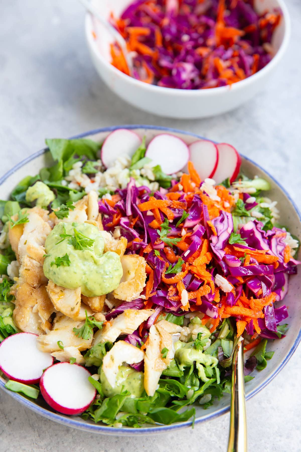 Fish taco bowl full of greens, rice, cabbage slaw, fish, and avocado crema.