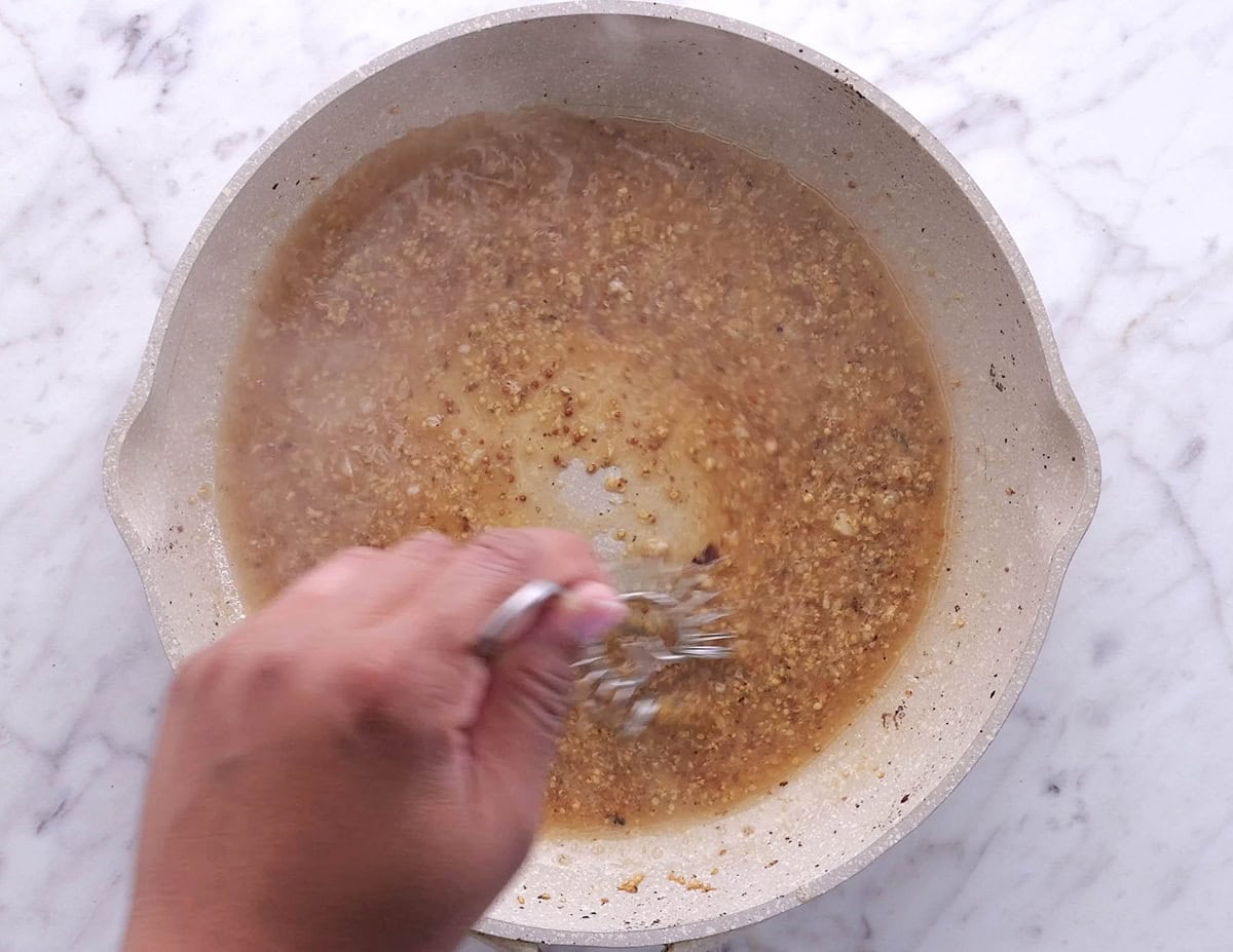Hand whisking sauce in a skillet to make dressing for potato salad.