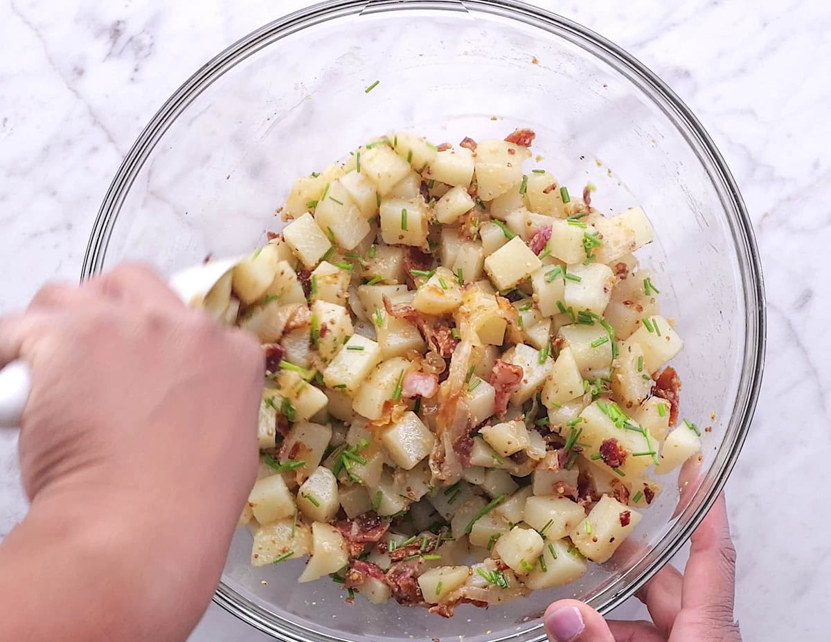 Hand mixing potato salad in a mixing bowl.