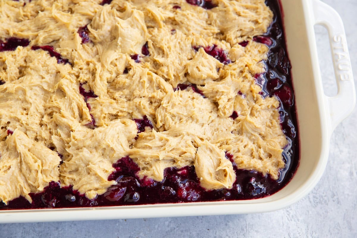 Casserole dish full of berry mixture with cake batter on top, ready to go into the oven.