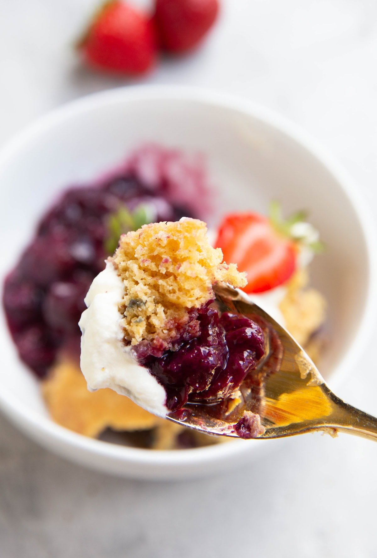 Spoon full of berry cobbler with whipped cream, ready to eat.