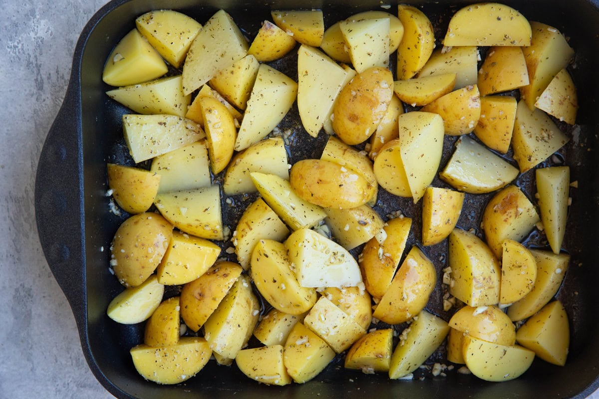 large casserole dish full of chopped potatoes drizzled in oil, salt, pepper, and fresh garlic.