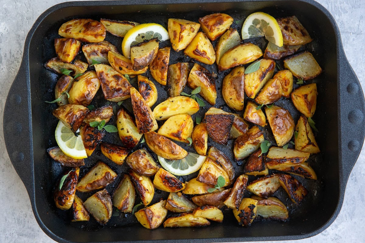 Baking dish full of roasted potatoes with lemon slices and fresh oregano.