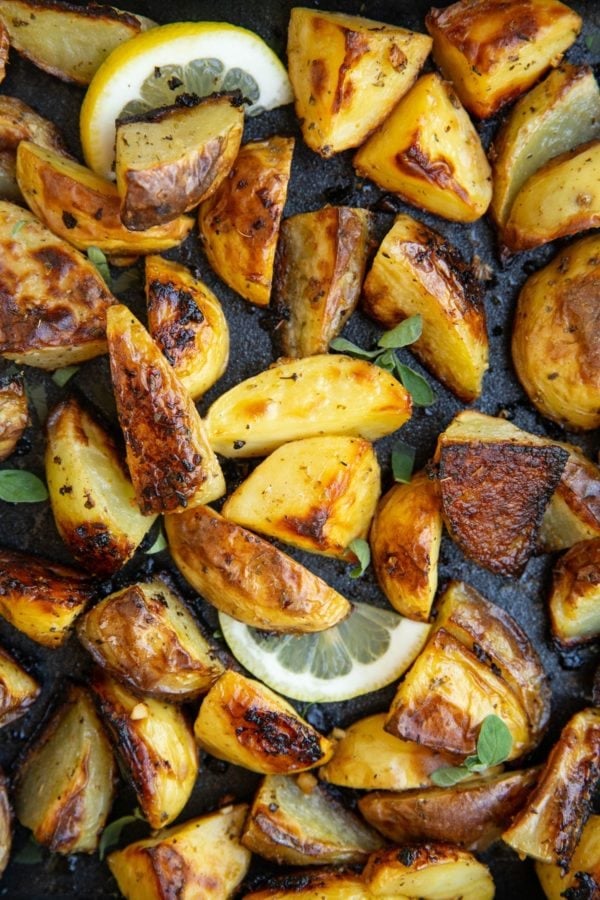 Roasted potatoes in a baking dish with lemon slices and fresh oregano.