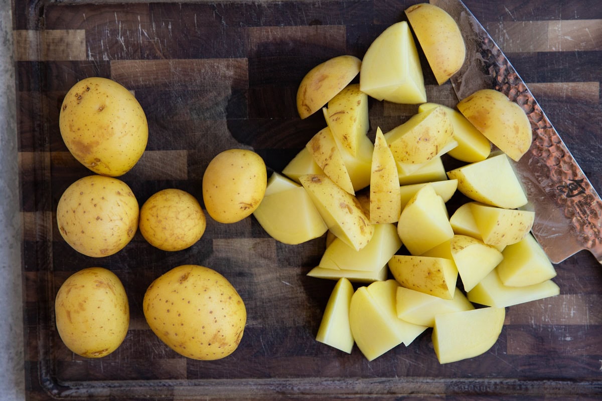 Wooden cutting board with Yukon gold potatoes being chopped up.