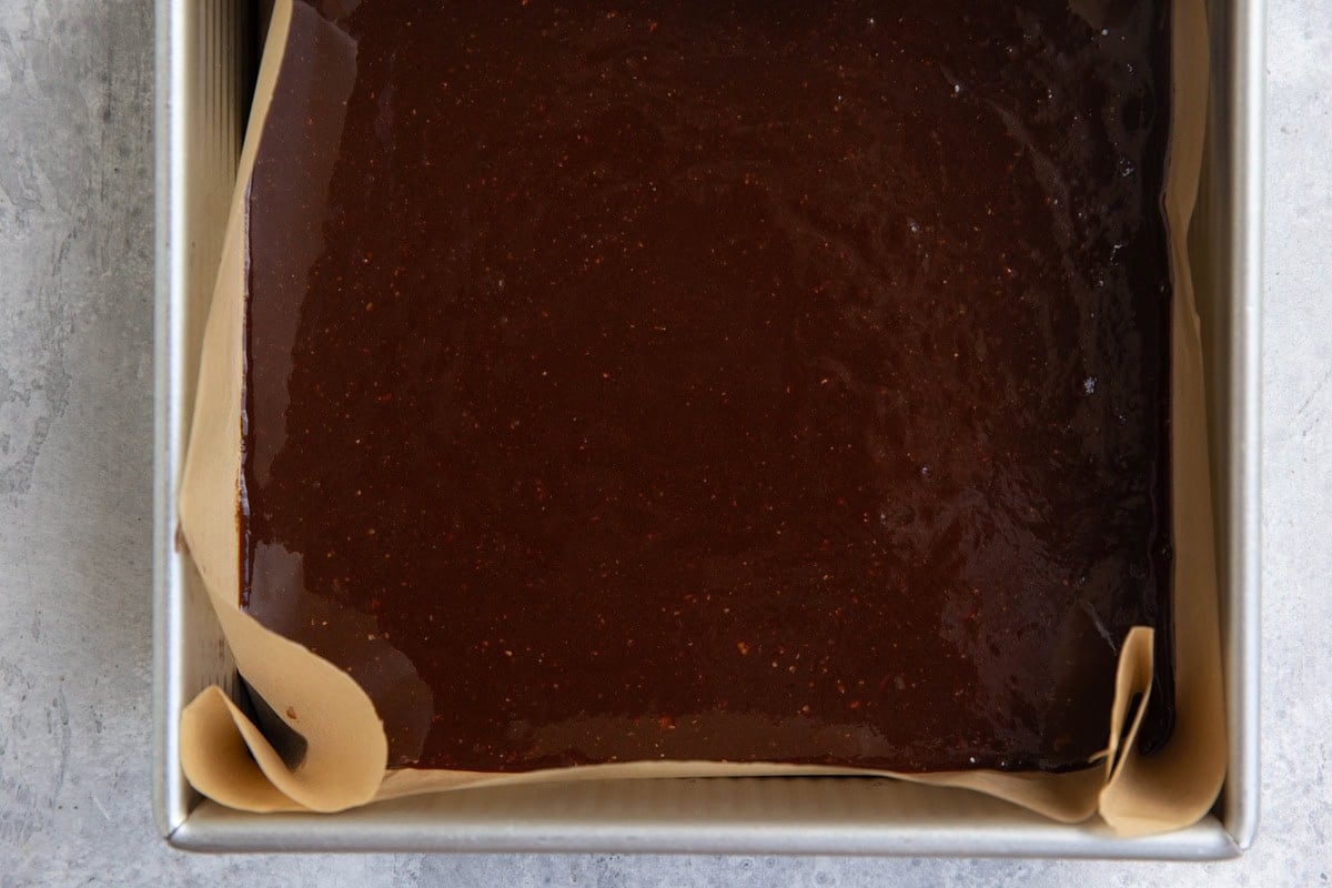 Baking pan lined with parchment paper with brownie batter inside.