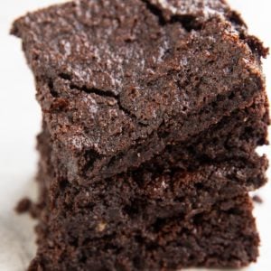 Stack of oat flour brownies on a white background so you can see the crinkle top and the fudgy insides.