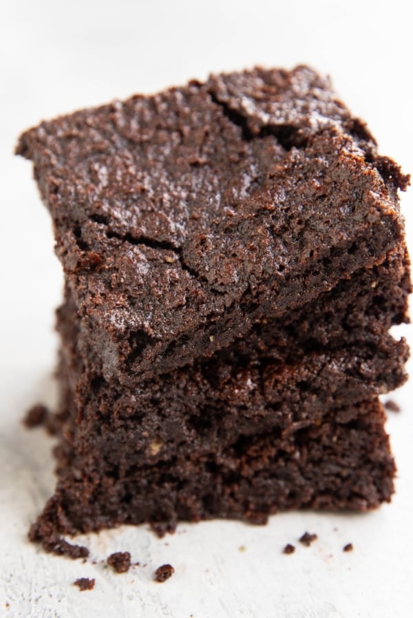 Stack of oat flour brownies on a white background so you can see the crinkle top and the fudgy insides.